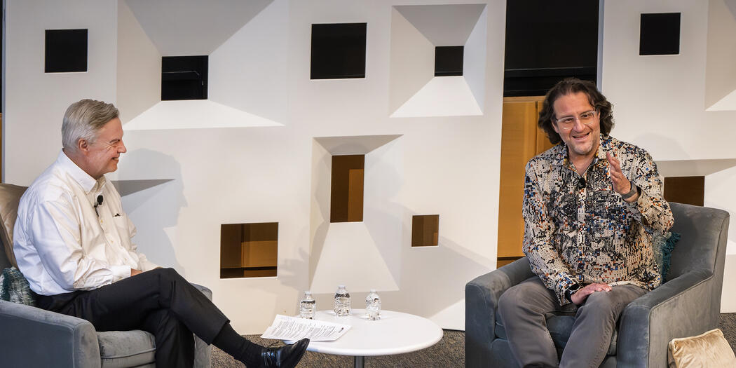 Two men sitting across from each other addressing a crowd.