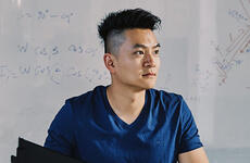 Jack Yao sits at his desk in front of a whiteboard with equations on it