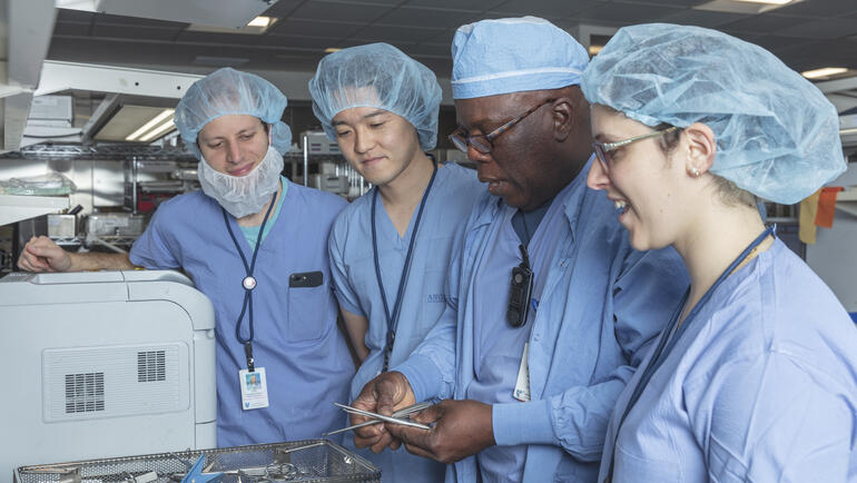 Students and host wearing surgical outfits looking at surgical tools. 