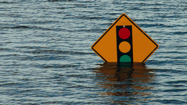 A photo of a street sign depicting an approaching stop sign. The sign is nearly underwater due to a flood.