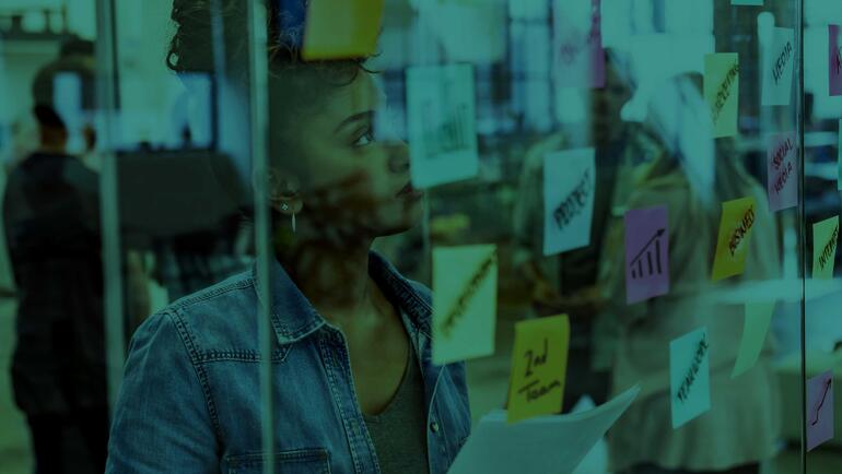 Black woman standing at glass wall looking at post-it notes