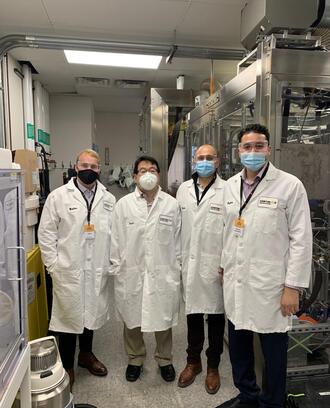 Three H-Lab students and Bayan Takizawa posing in lab coats at Continuus Pharmaceuticals