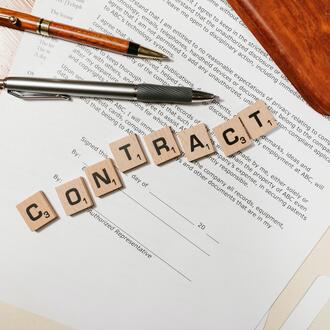 Image of a contract and office supplies, with the word "Contract" spelled out in Scrabble tiles