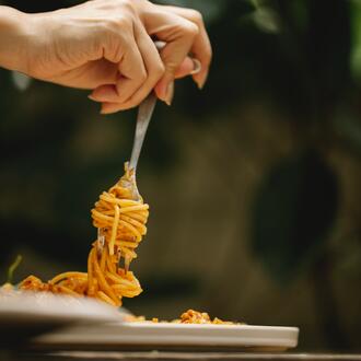 Image of a hand holding a fork with spaghetti swirled around it