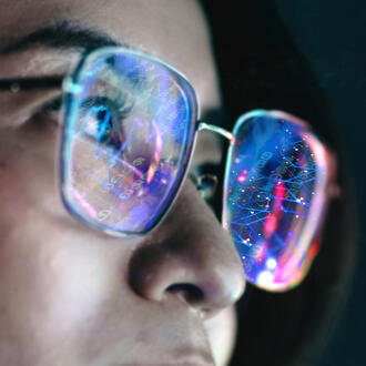 A person wears eyeglasses with lenses that reflect abstract digital art
