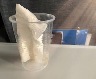 Plastic cup with paper napkin inside sitting on airplane tray table