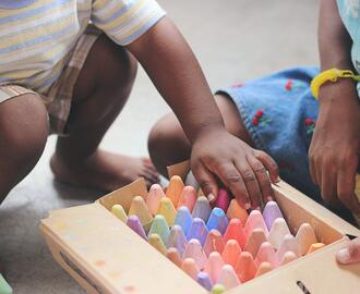 Two children kneeling over a wooden box of colorful chalk