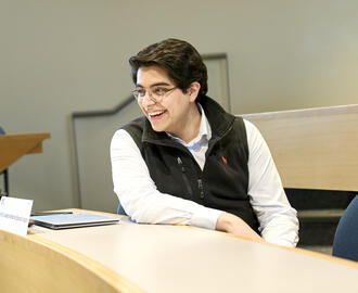 Sandro Joseph sitting in a classroom, a closed laptop in front of him, he is smiling