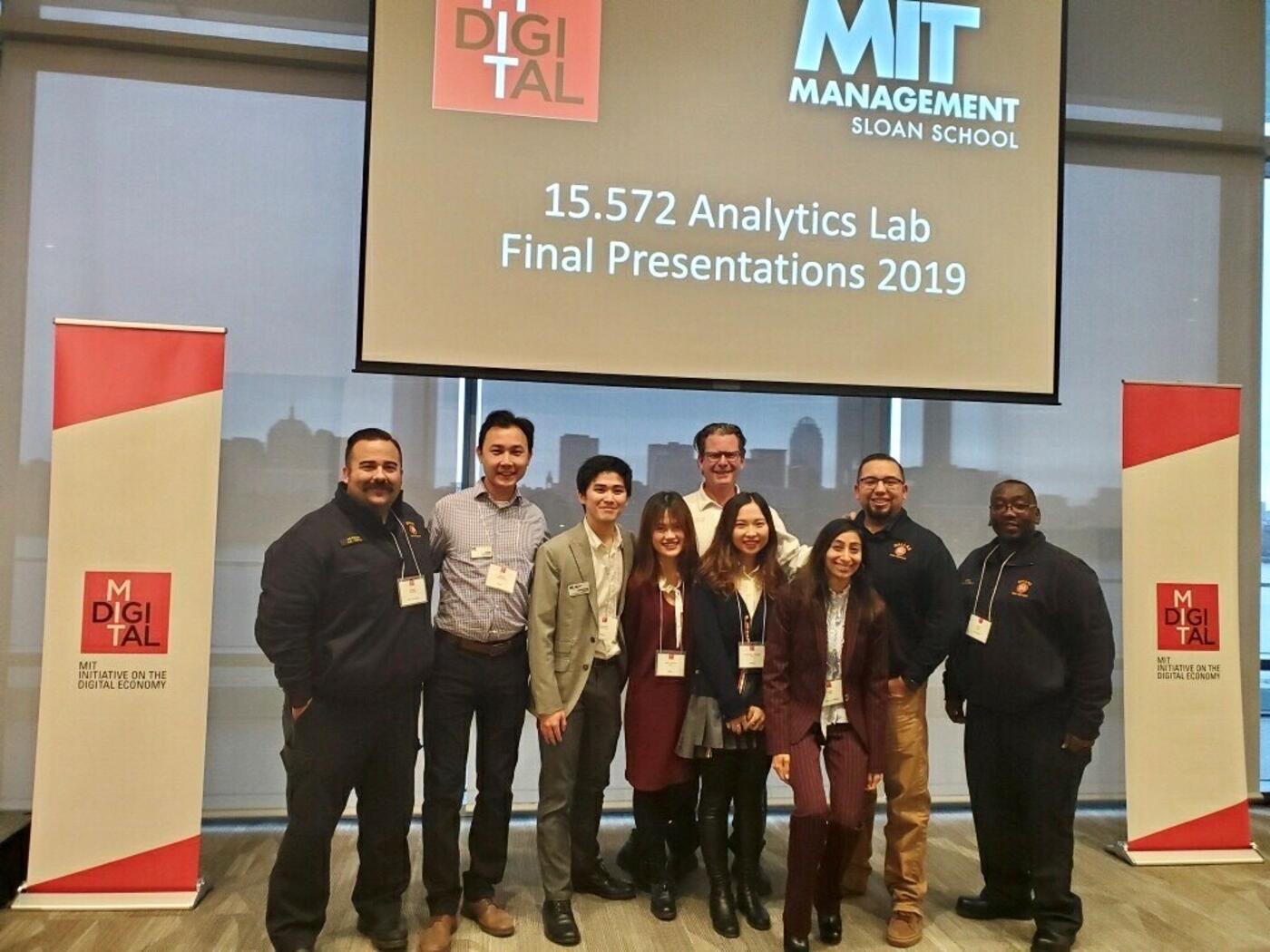 A-Lab Team and Dallas Fire and Rescue Department posing in front of presentation screen in Samberg Conference Room, MIT Sloan campus