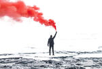 a lone figure stands on a snow-covered rocks, holding a red smoke flare