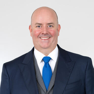 Man smiling wearing a dark blazer and a bright blue tie