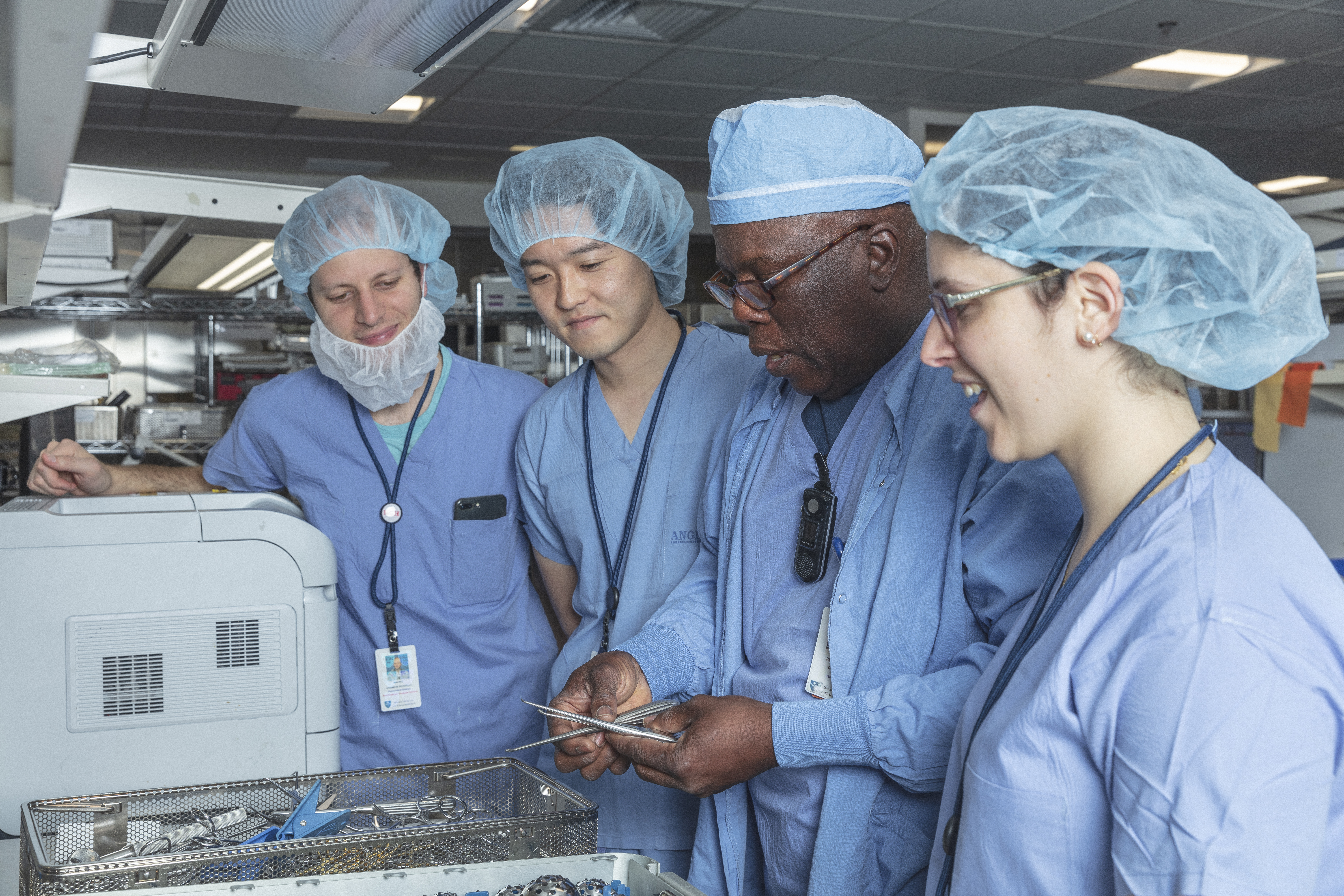 Students and host wearing surgical outfits looking at surgical tools.