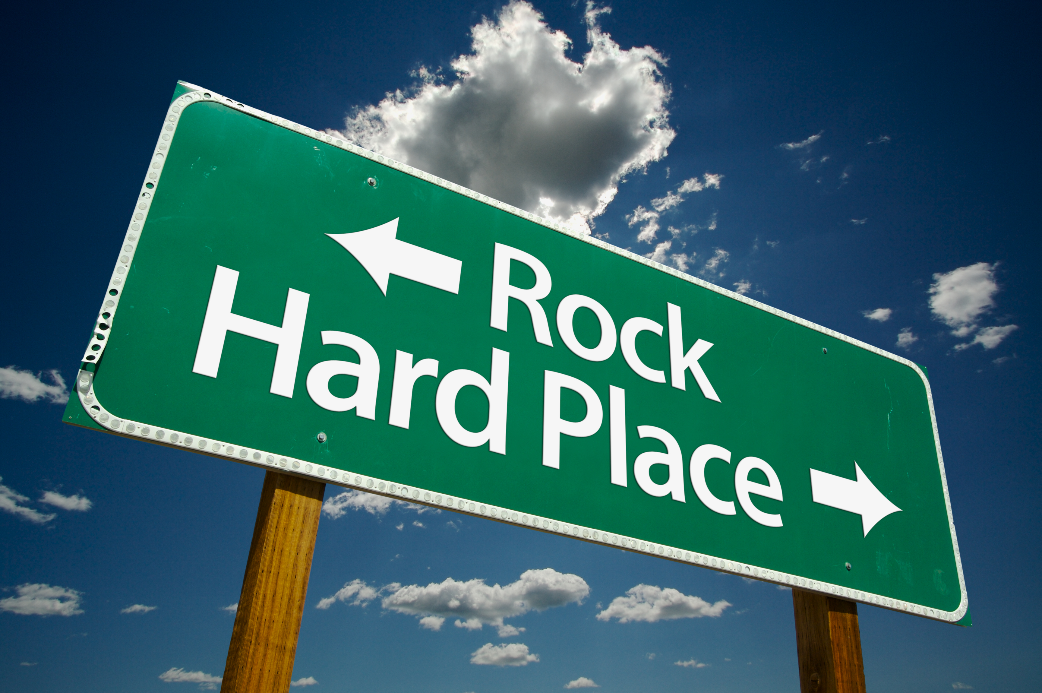 Green sign with words arrowing pointing left next to words reading "Rock" and arrow pointing right next to words "Hard Place"