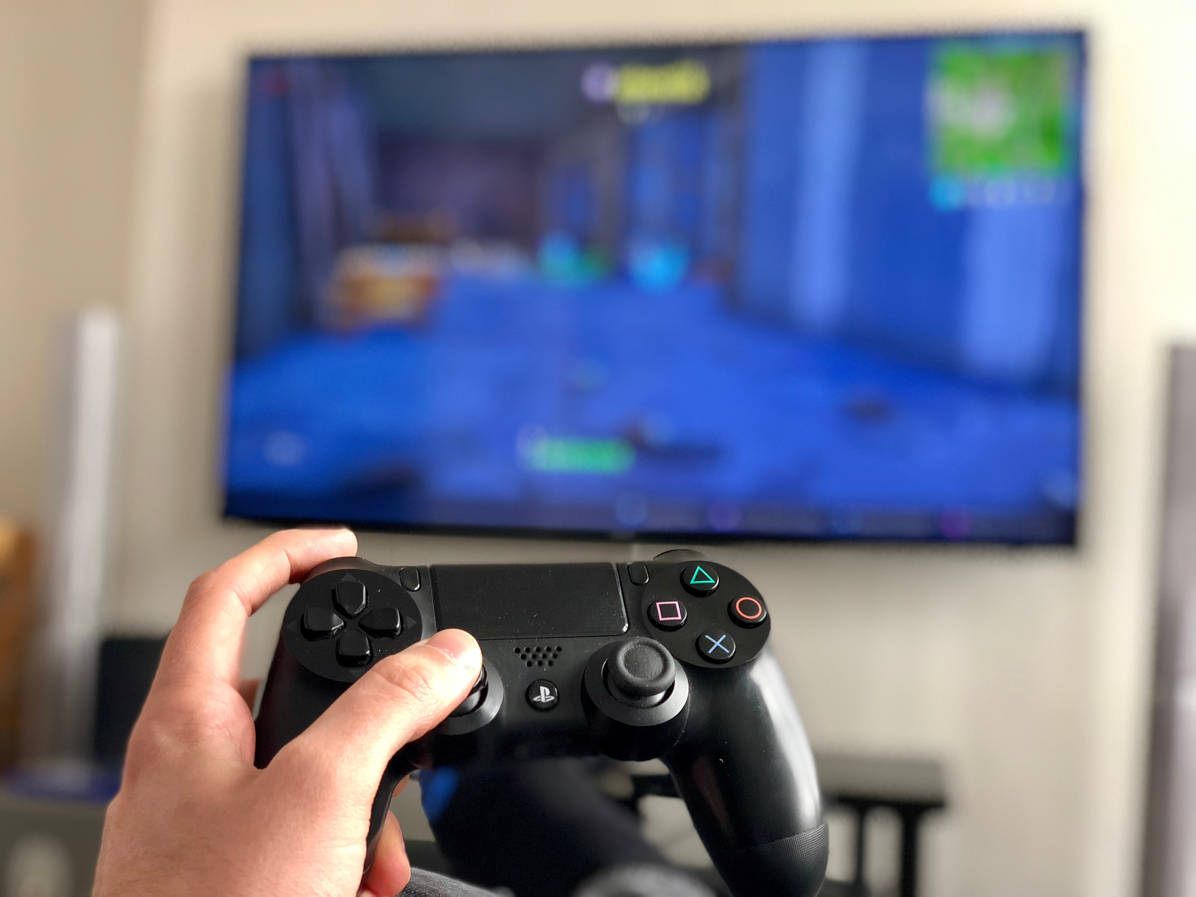 hand holding playstation remote control and blurred TV screen