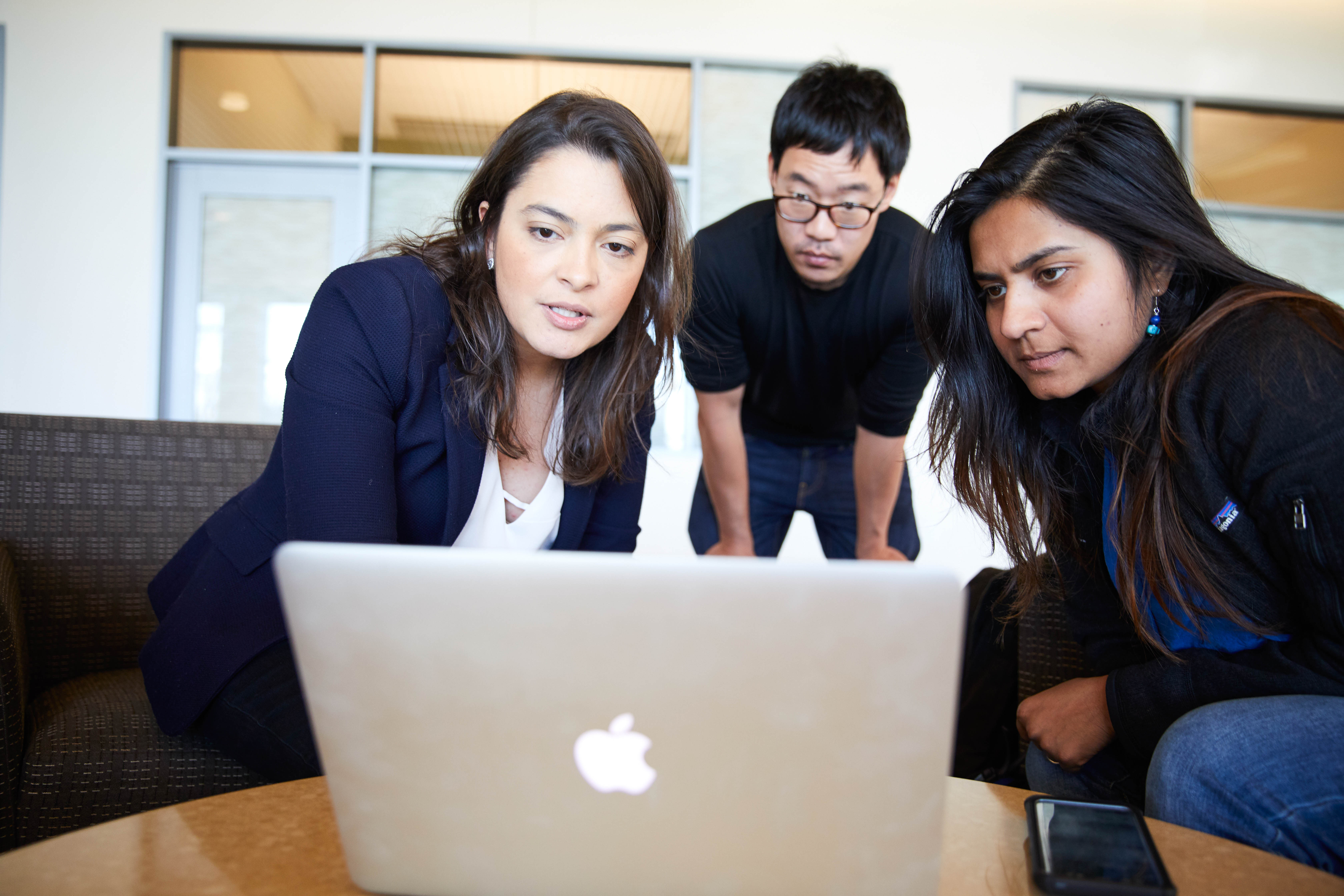 Two women and man sitting in front of a laptop conversing