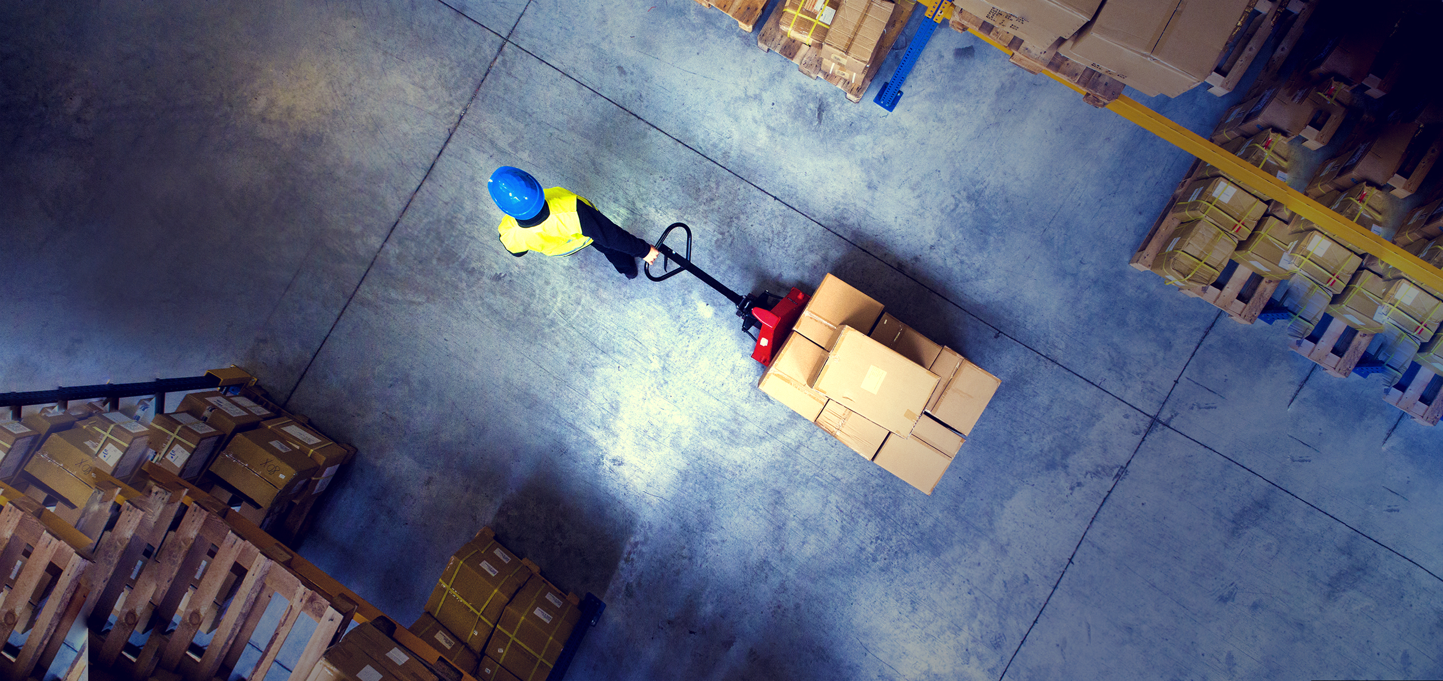 a warehouse worker pulls a wheeled pallet of boxes through a corridor