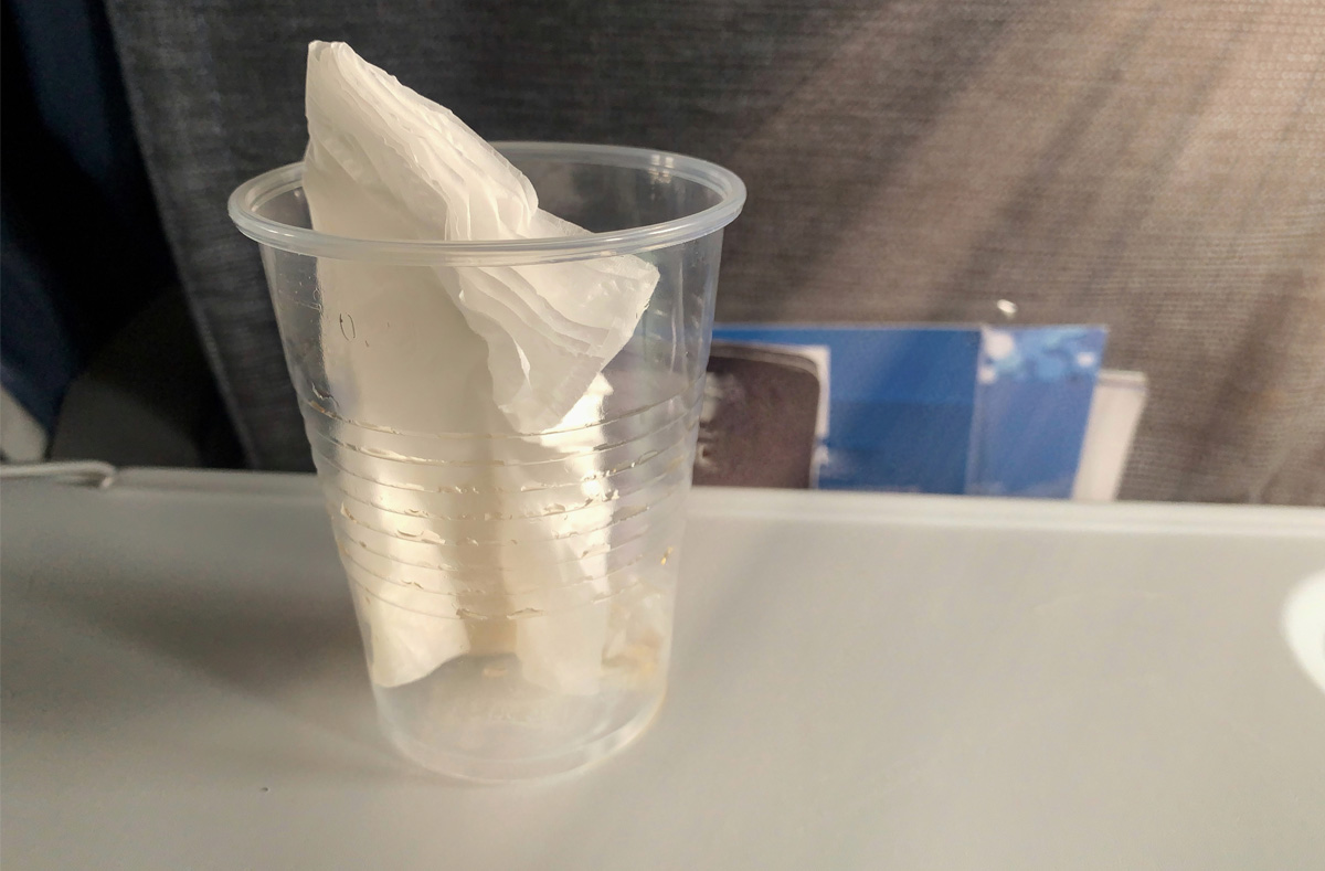 Plastic cup with paper napkin inside sitting on airplane tray table