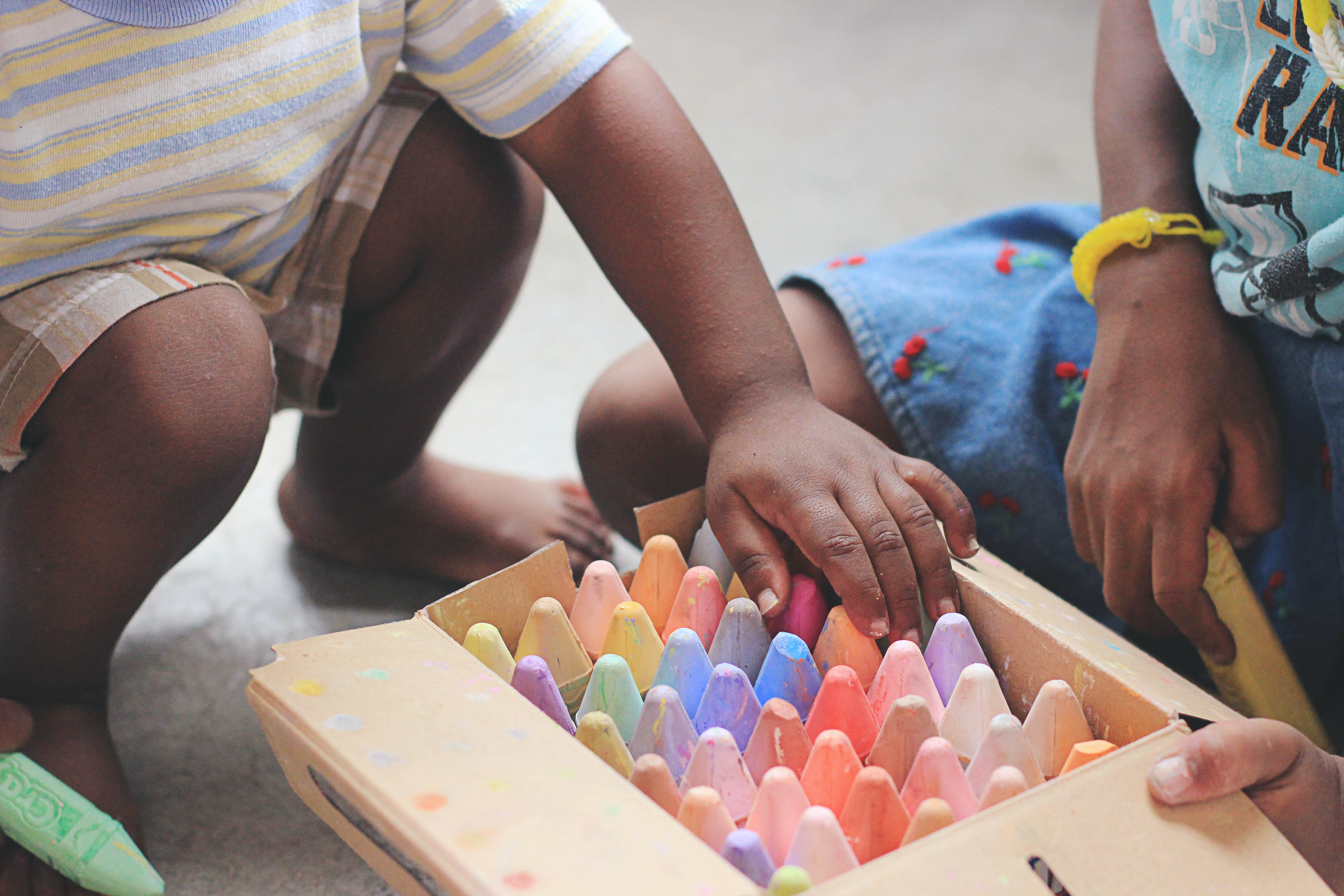 Two children kneeling over a wooden box of colorful chalk