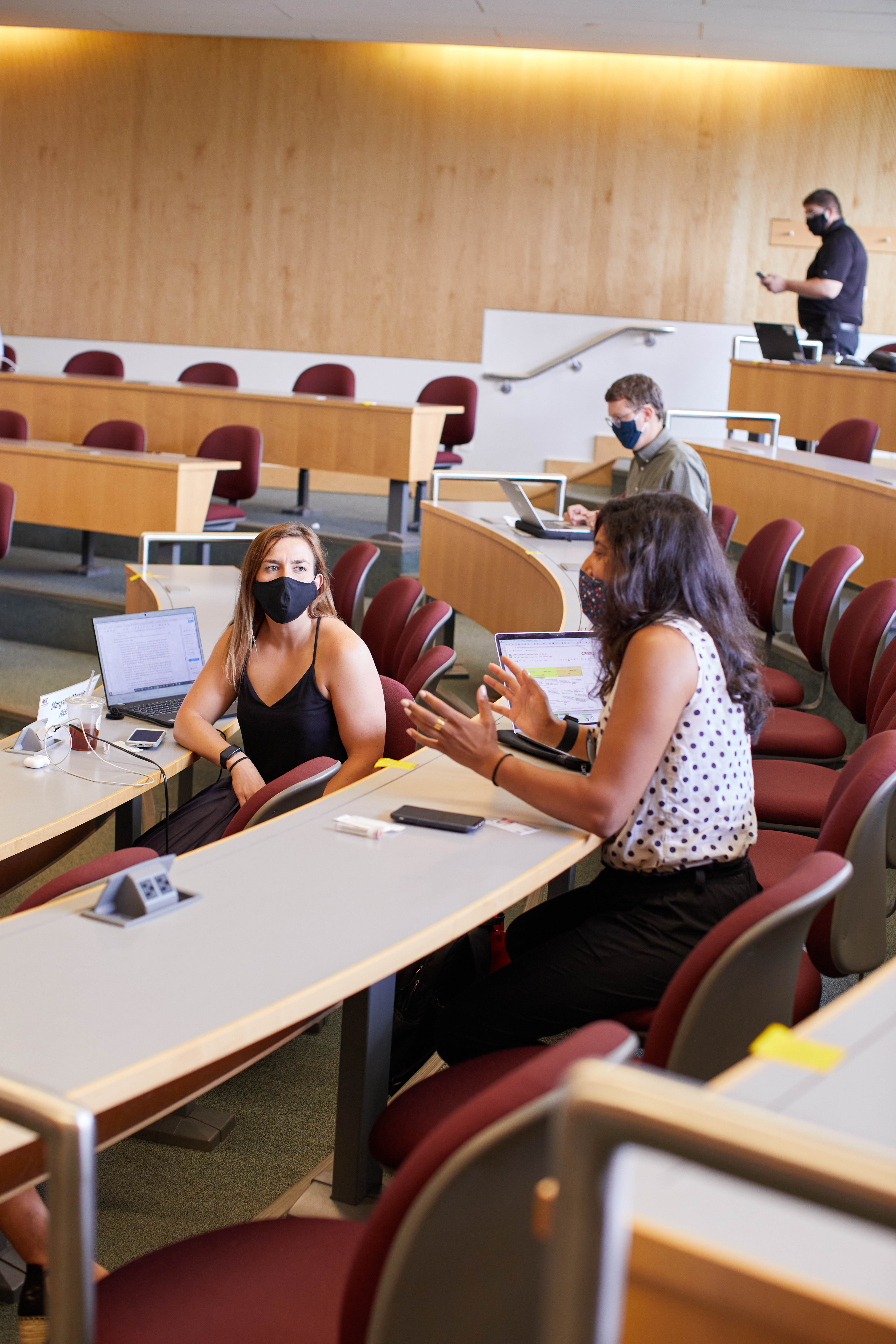 Two masked women talking in large Sloan classroom