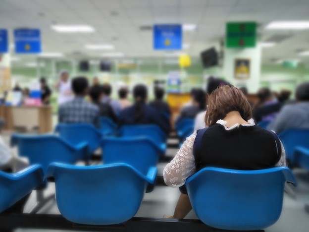 hospital waiting room with many patients in blue plastic chairs, seen from back