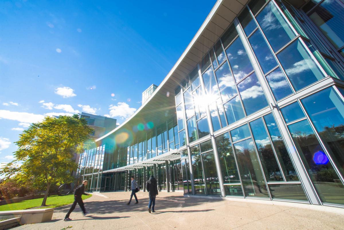 The outside of the MIT Sloan building E-62, on a sunny day with people walking near it