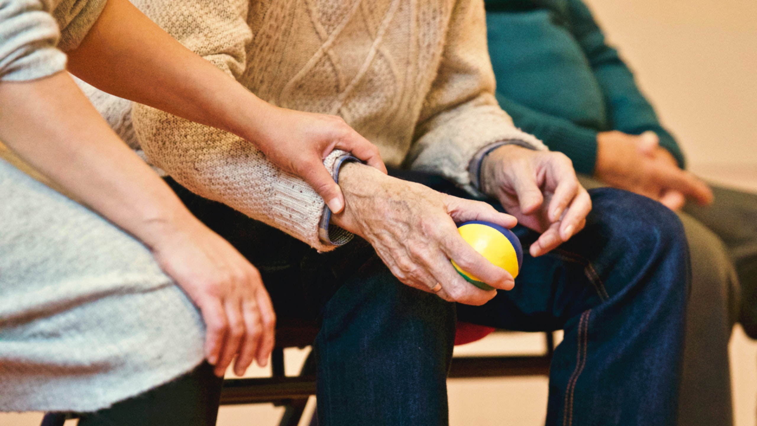 Nursing assistant aiding an elderly man holding stress ball