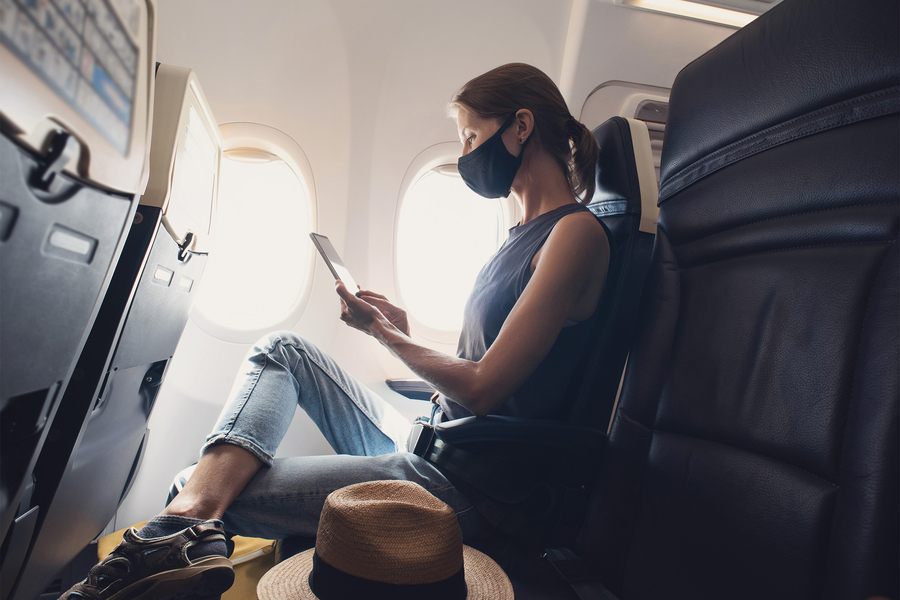 A masked airline passenger reads during their flight.