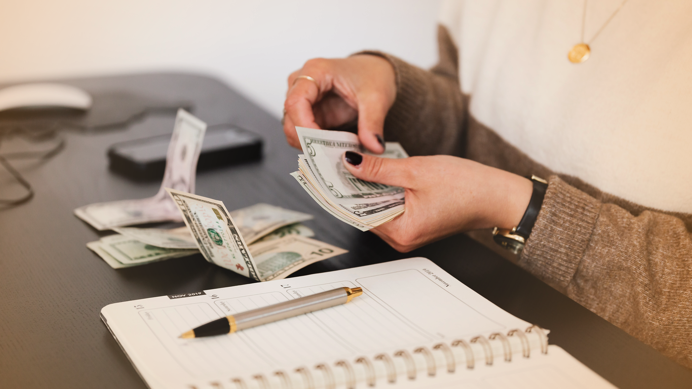 Person counting money with a pen and notebook nearby