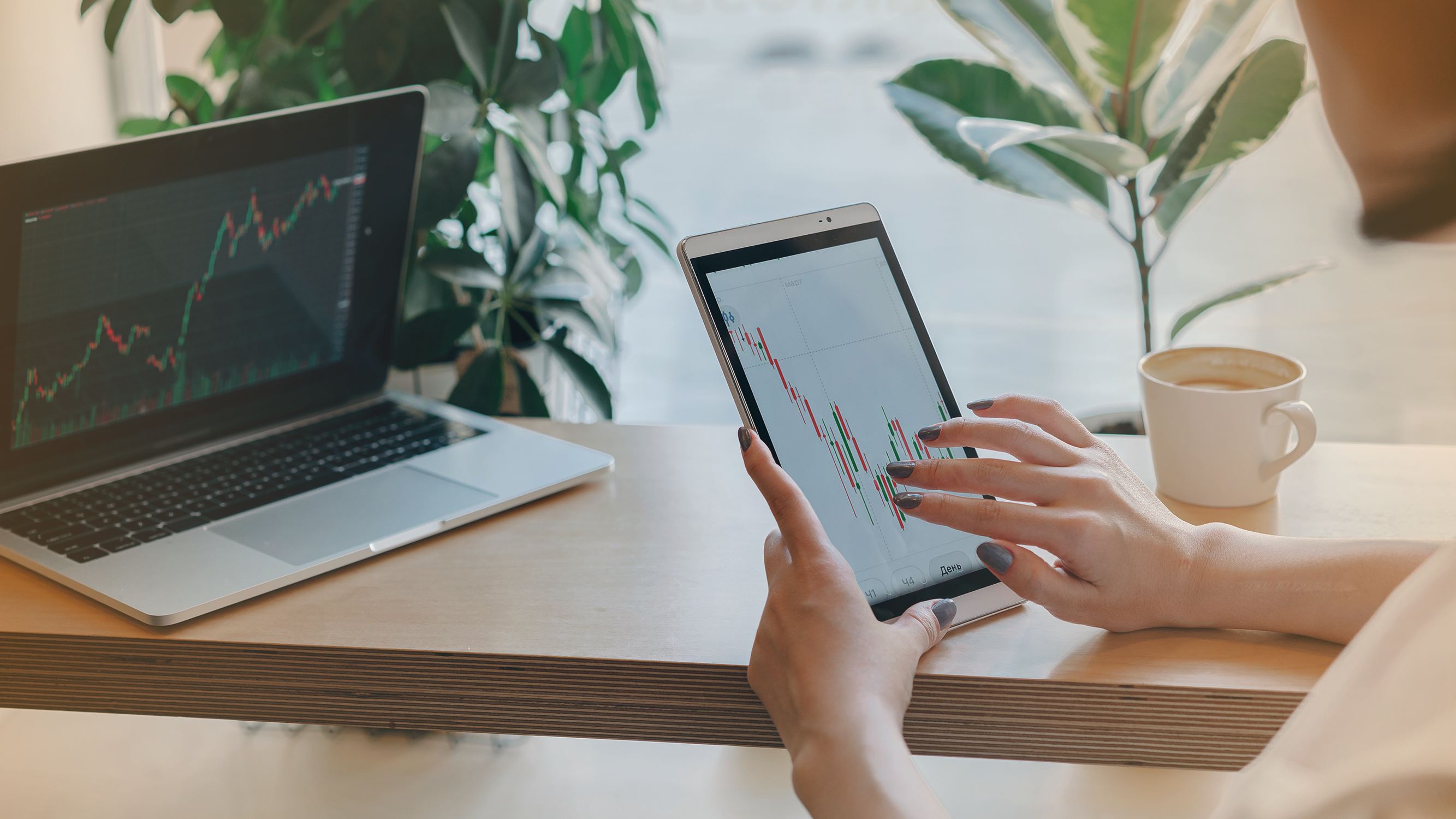 Person working on iPad and laptop looking at stock charts