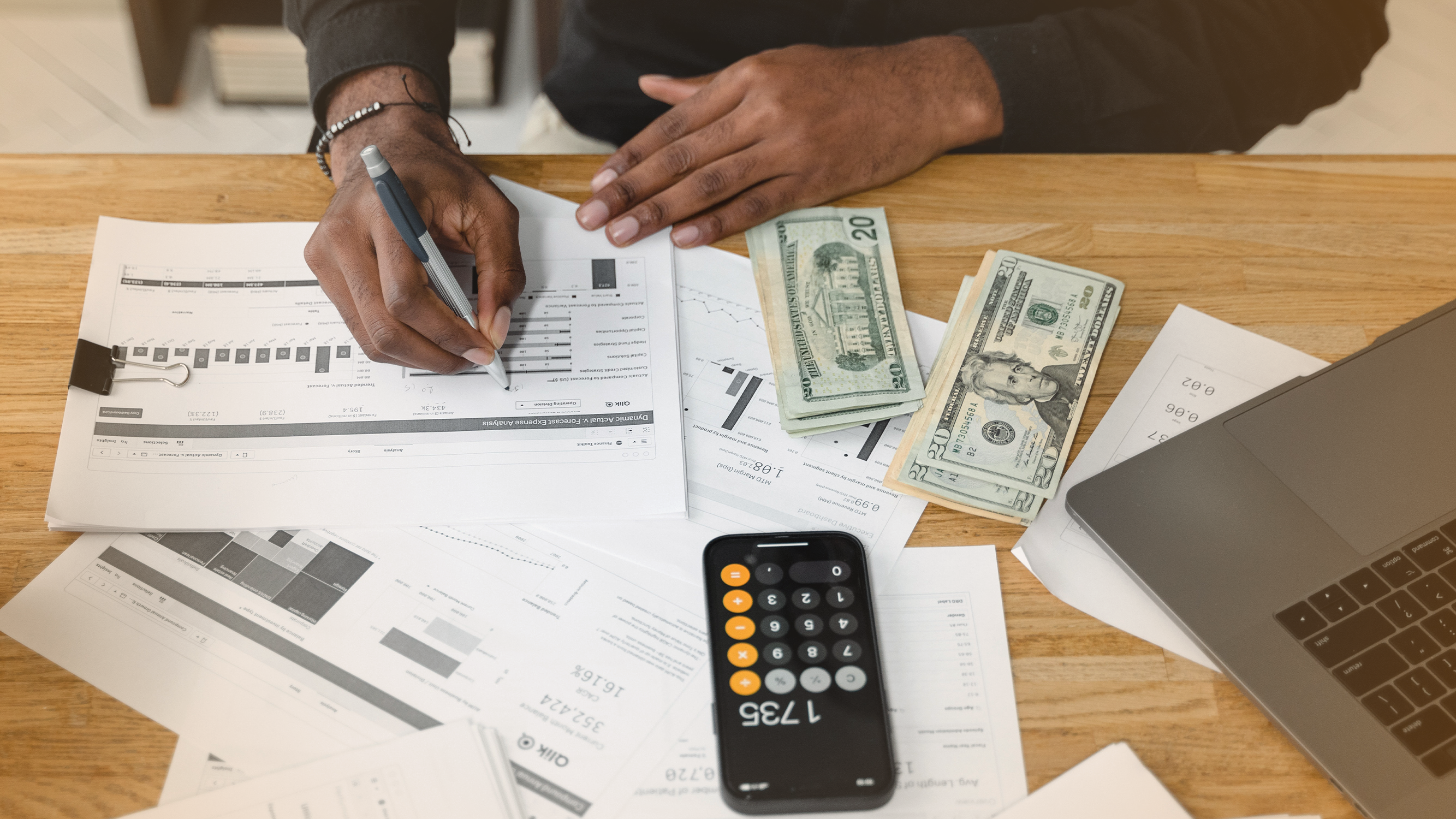 Person working with charts and cash, and a calculator at a table