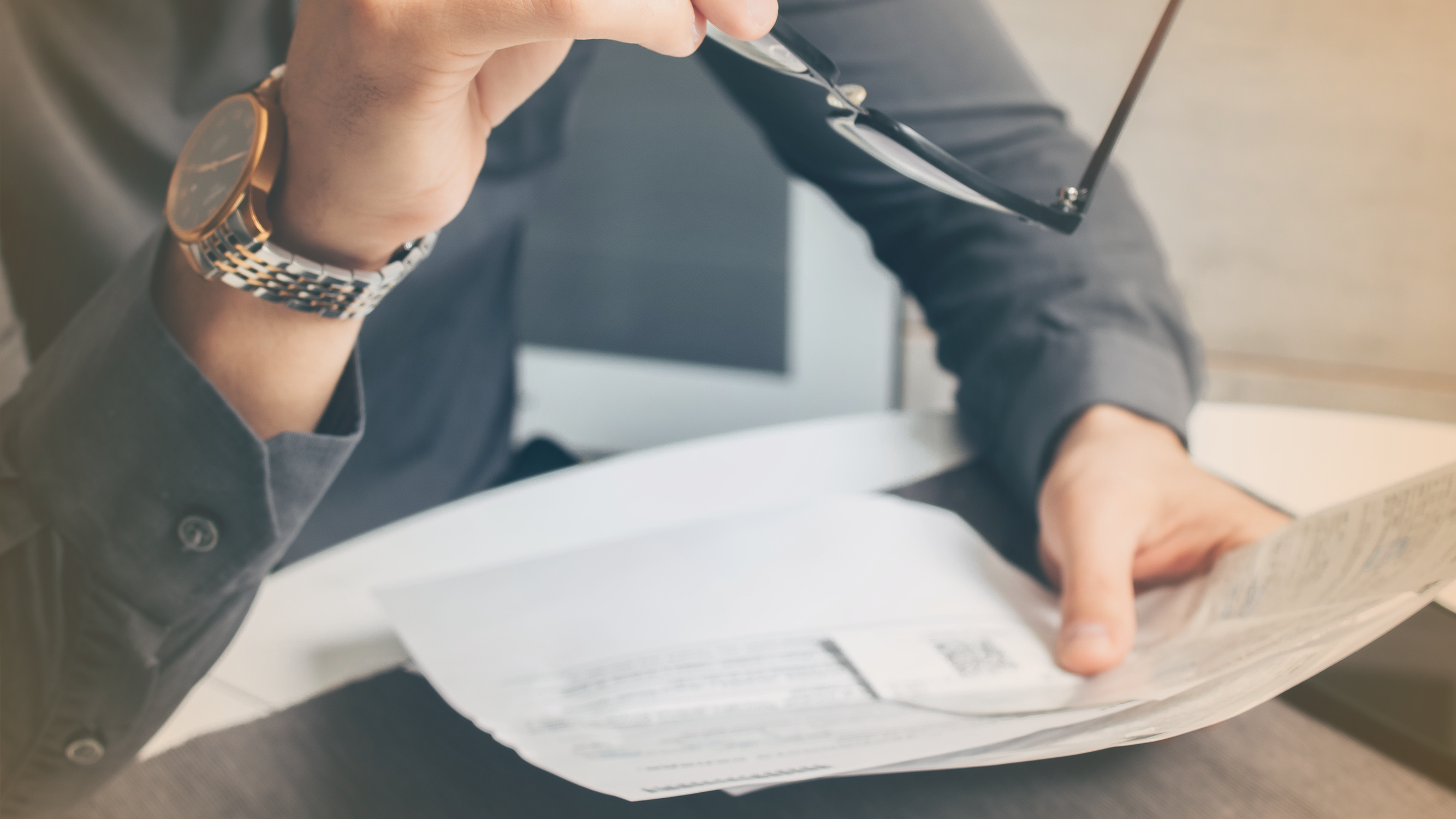 Person looking at banking statements holding glasses, relating to income risk and earnings