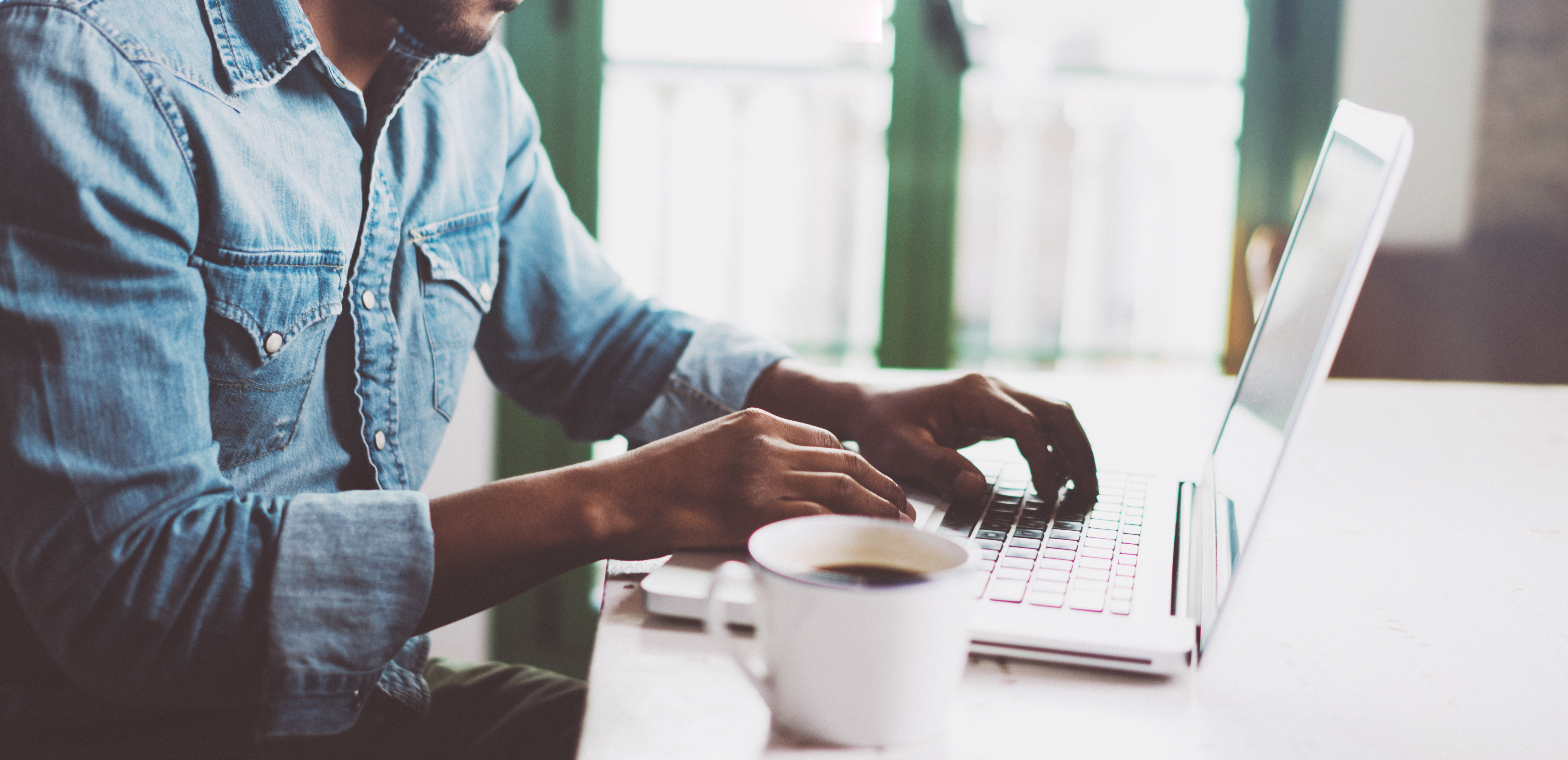 Person sitting at laptop with cup of coffee.