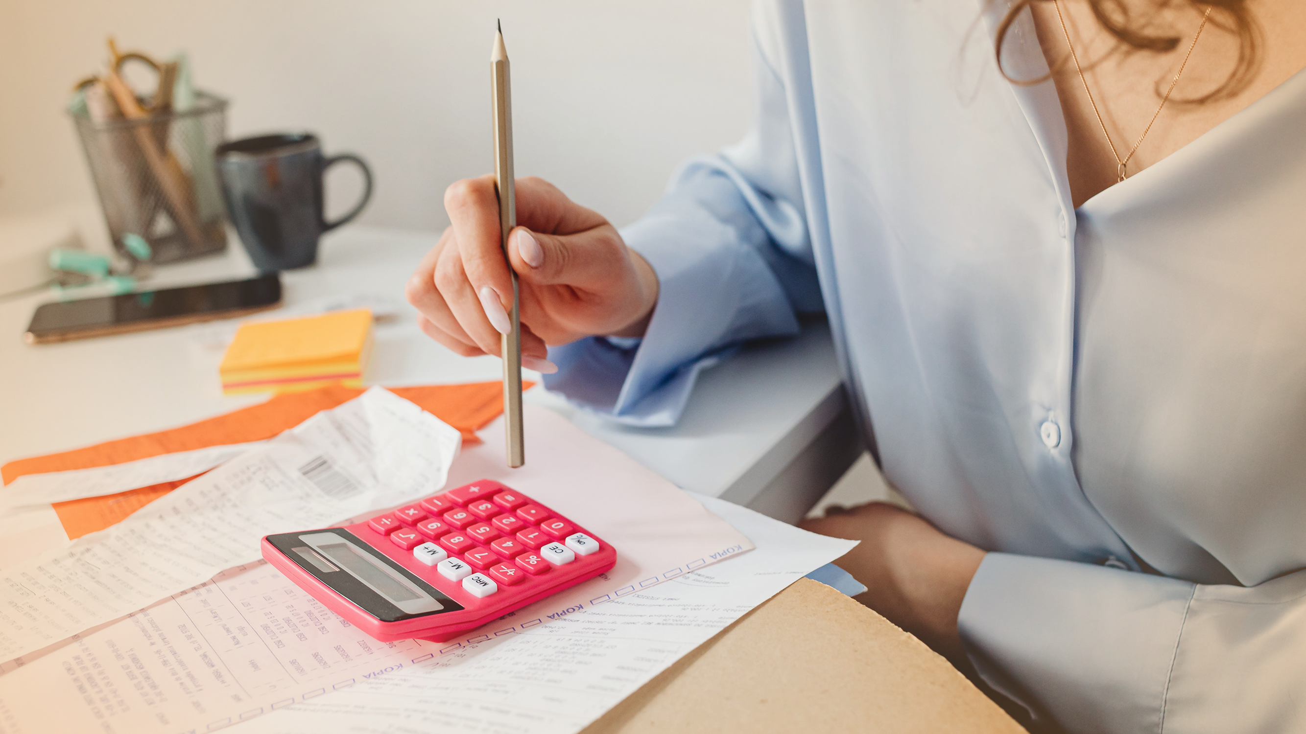 Person working with calculator and paper bills, relating to household debt and consumption
