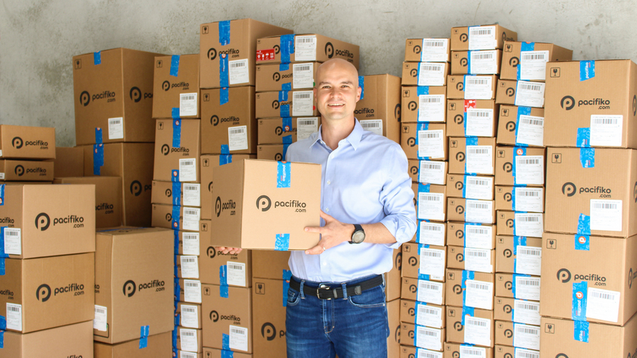 Man holds a shipping box in front of large stacks of shipping boxes