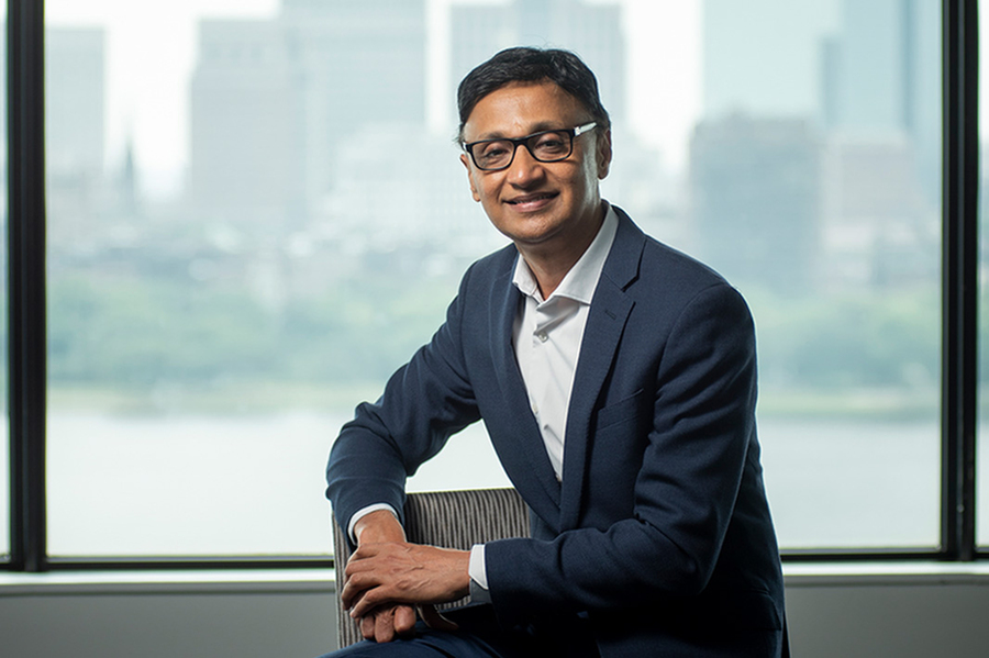 A man in a suit poses for a photo in front of a window overlooking a river and cityscape