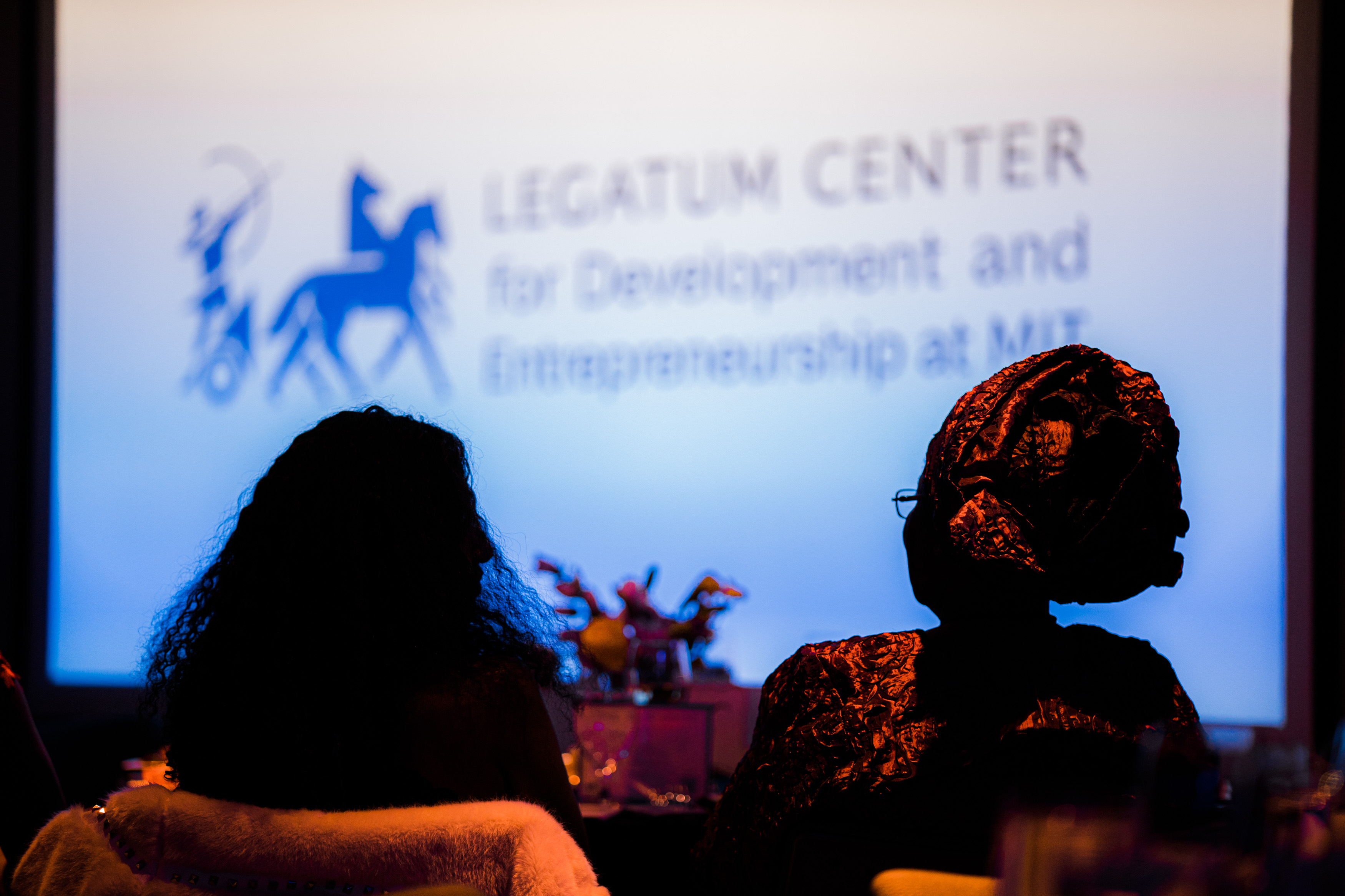 Two entrepreneurs silhouetted in front of a screen with Legatum Center on it