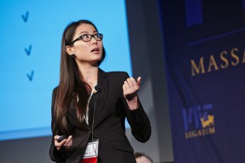 Female presenter standing in front of a blue screen with checkmarks