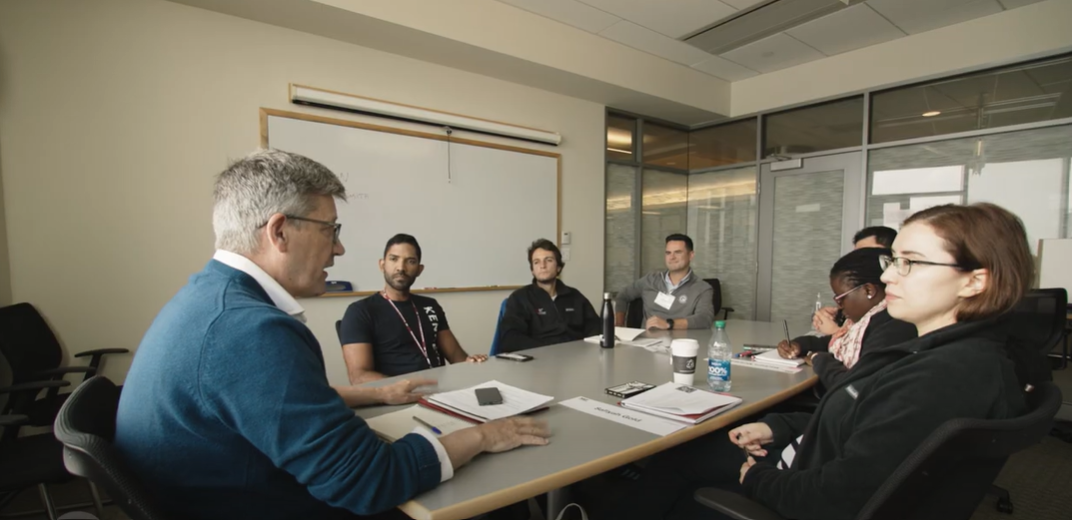 a man speaking to a group of people sitting at a table