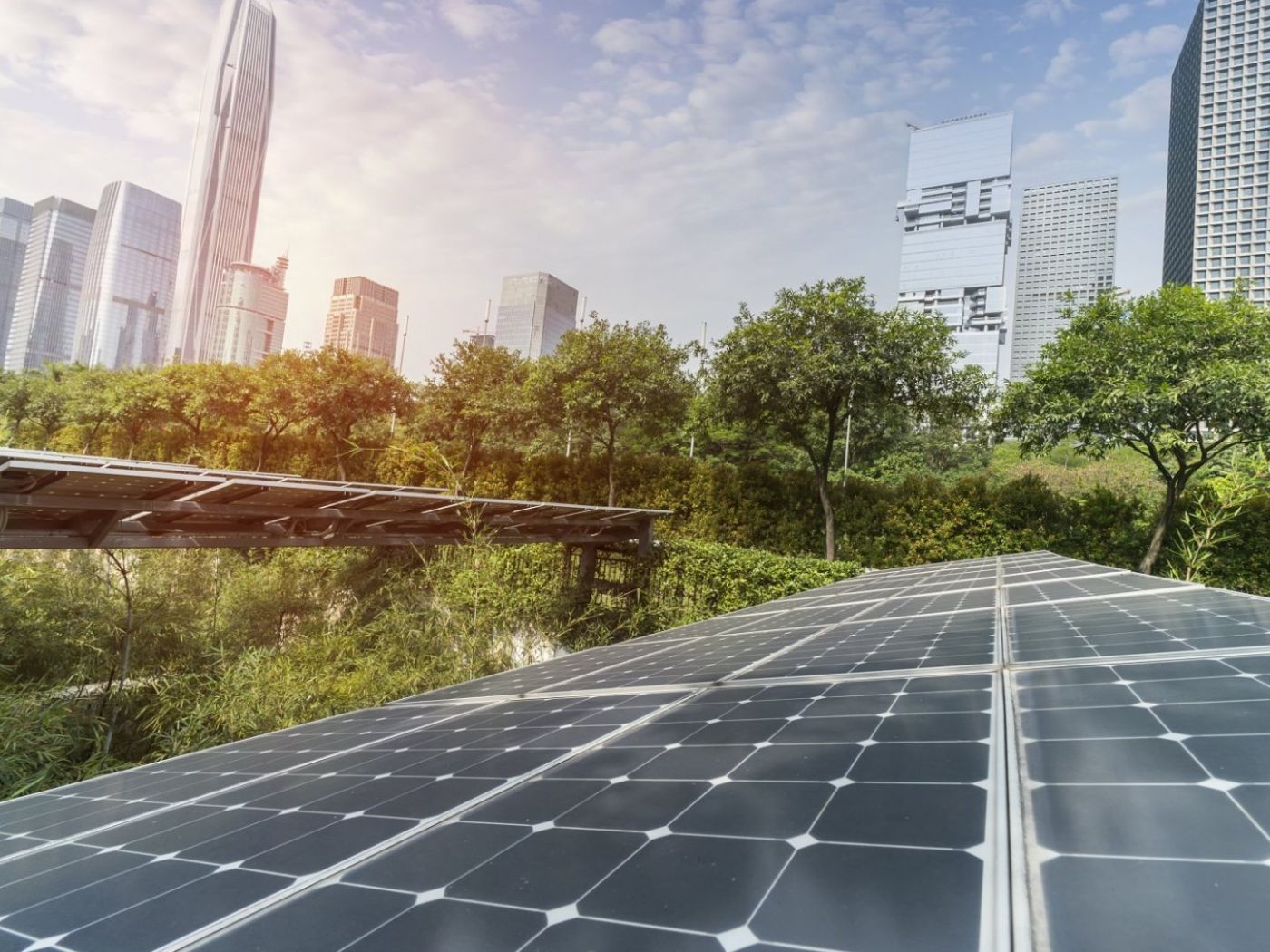 Solar panels in a city park, skyscrapers in the background against a blue sky.