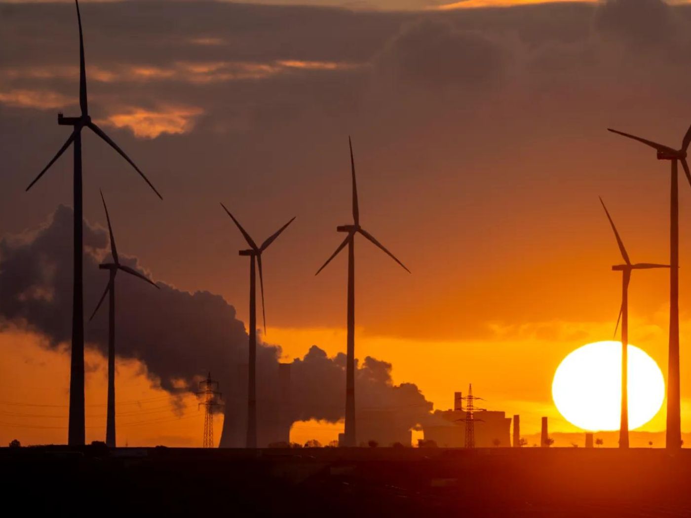 Steam rises from the coal-fired power plant with wind turbines nearby in Niederaussem, Germany, as the sun rises on Nov. 2, 2022.