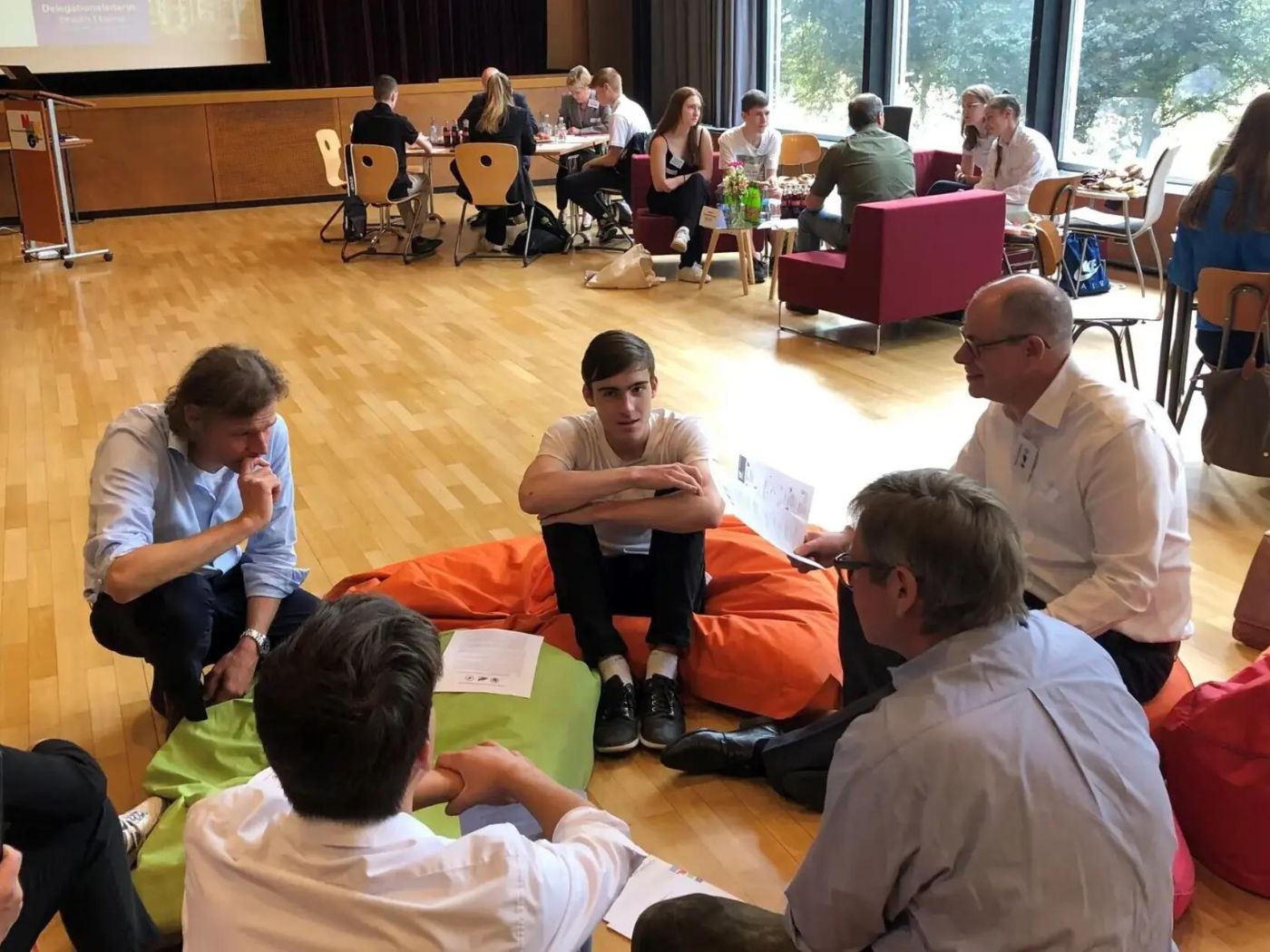 Five people sit in a circle on the floor in discussion in a gymnasium