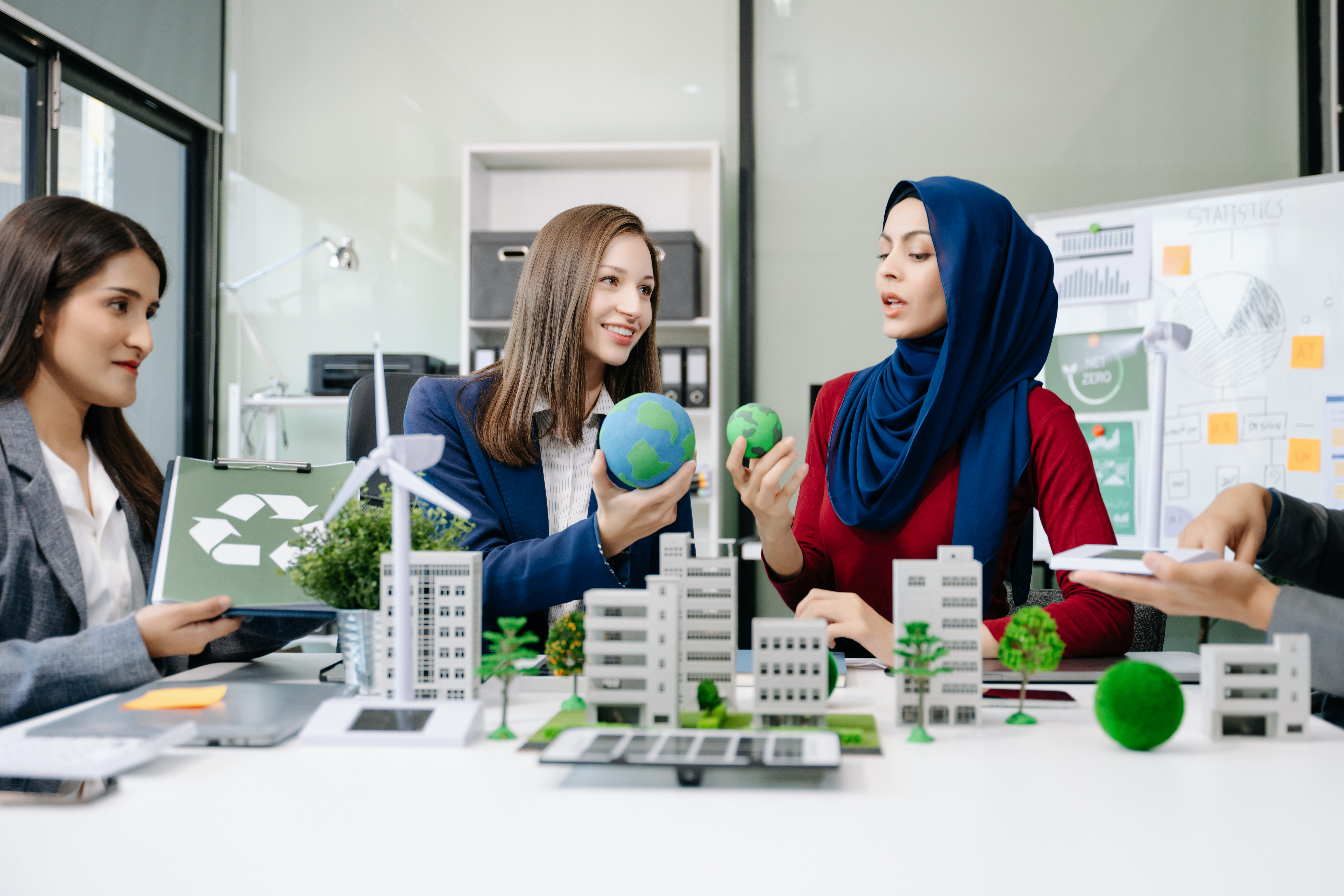 a group of women around a table speaking, two of them are holding small model globes