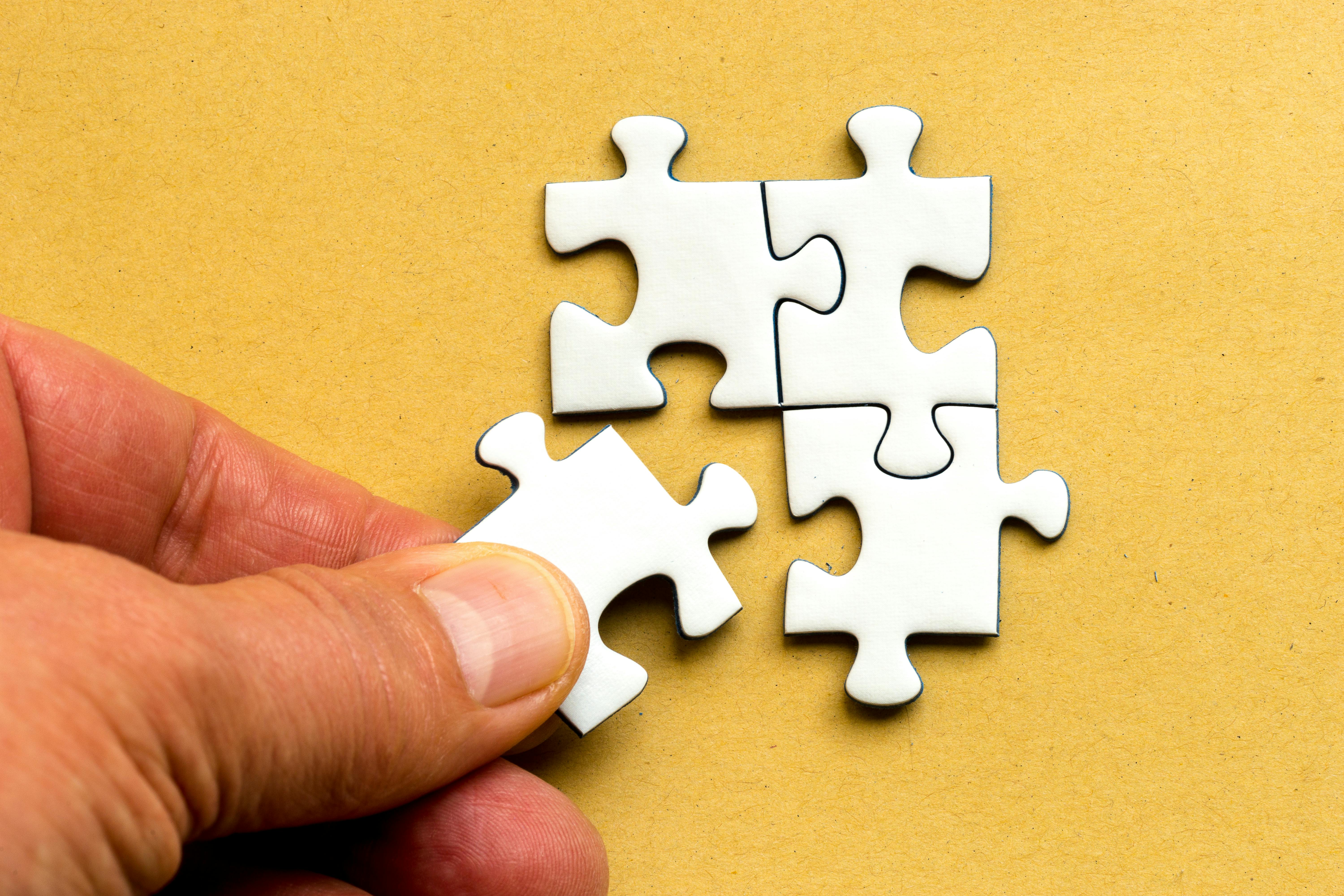 Image of a hand placing a fourth jigsaw puzzle piece next to three others
