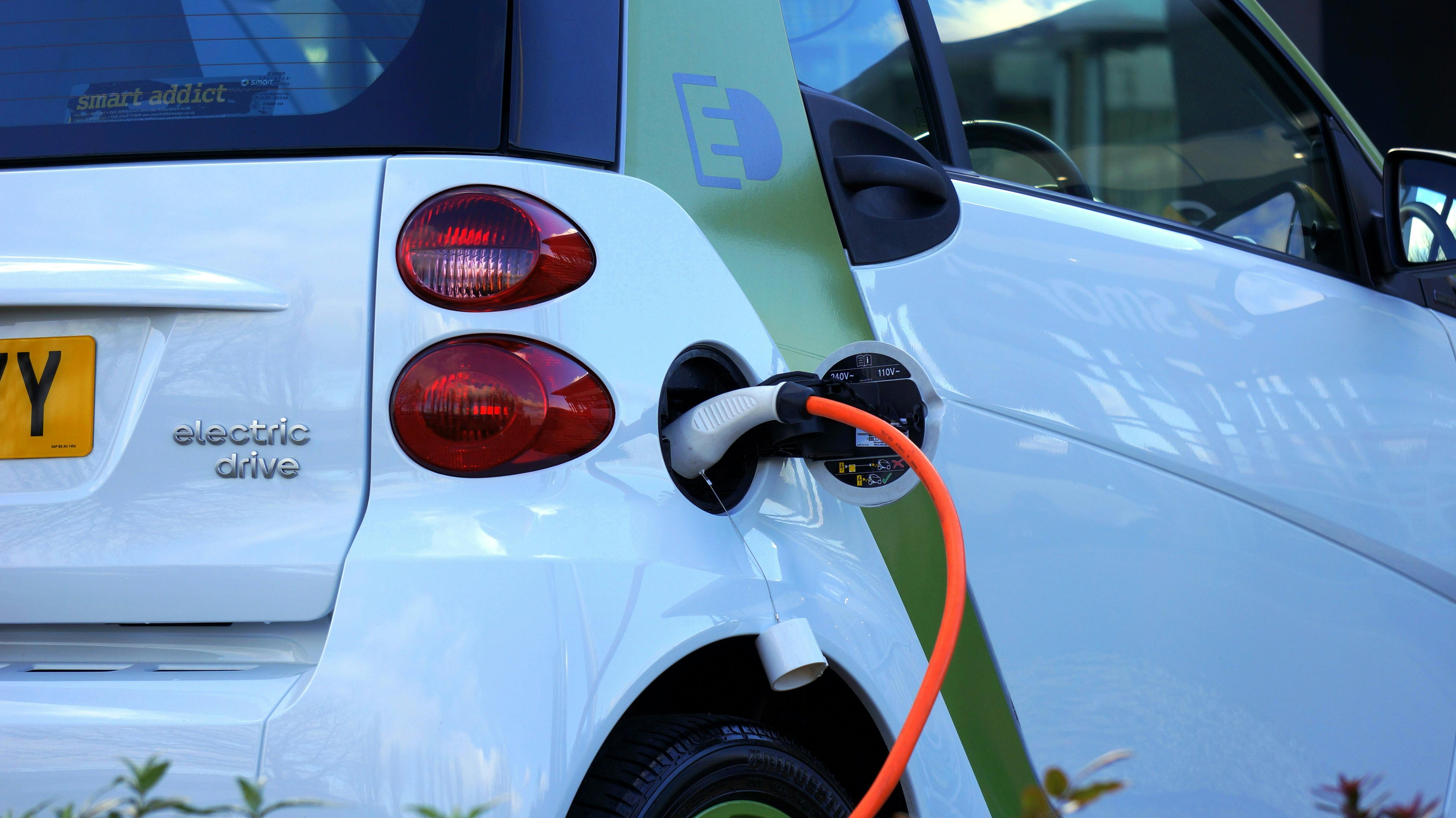Image of the back of an electric car charging, with a charger and cord visible
