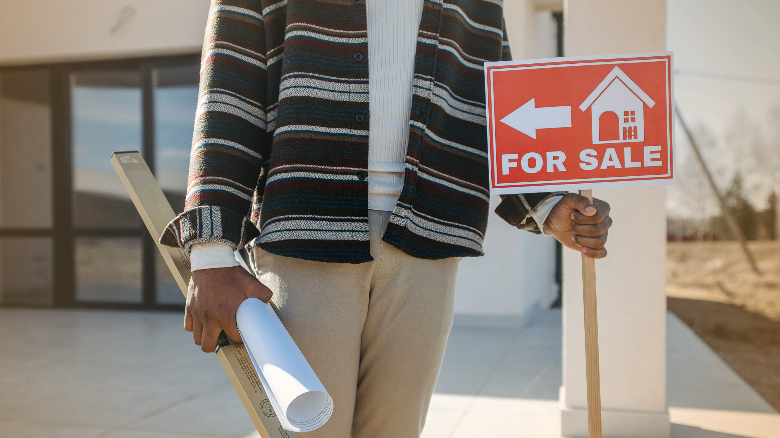 Person holding for sale sign in front of new house.