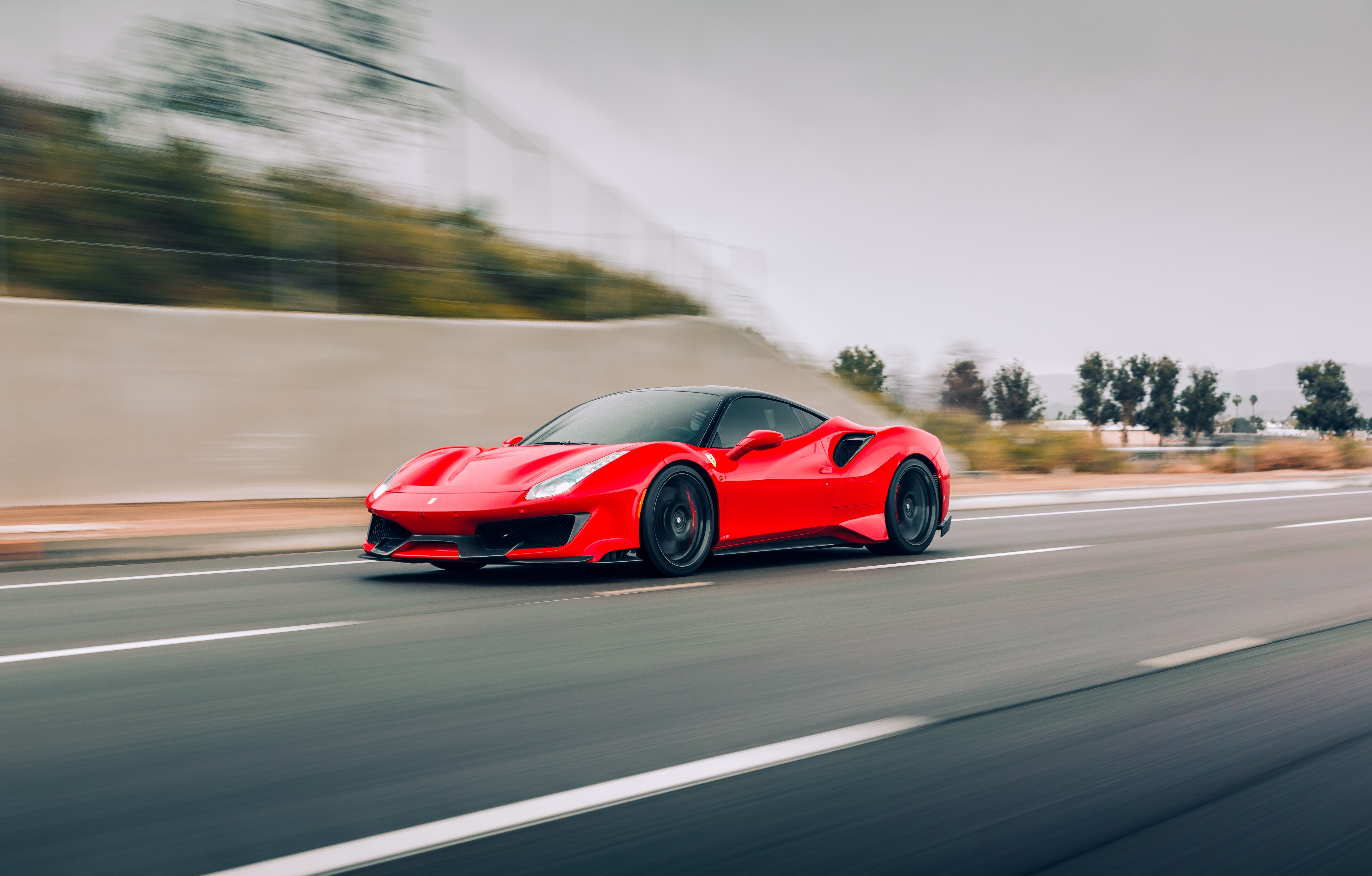 Red Ferrari on highway with blurred trees and coastal scene in background