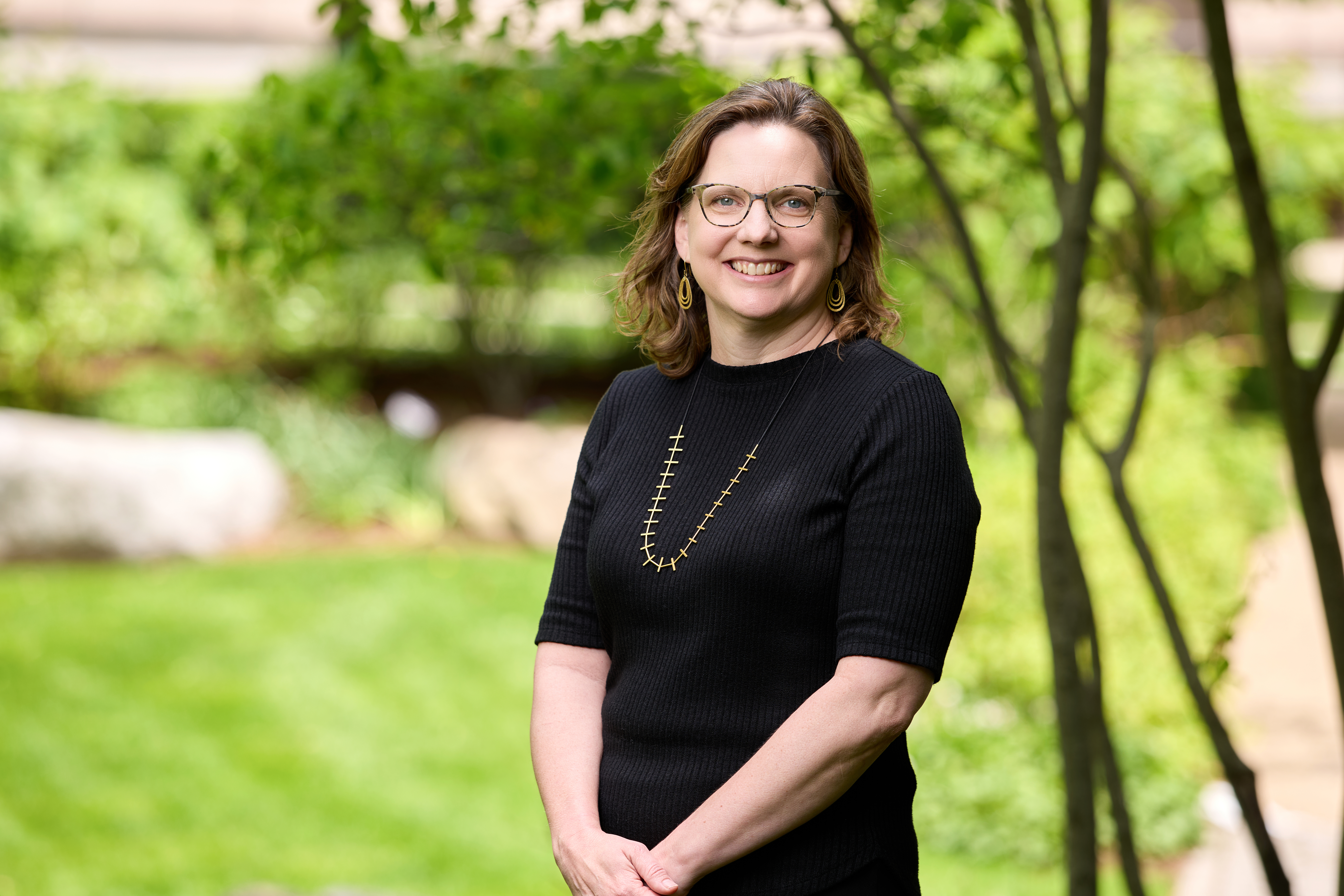 MIT Sloan Professor Erin L. Kelly standing outside, smiling, with greenery nearby