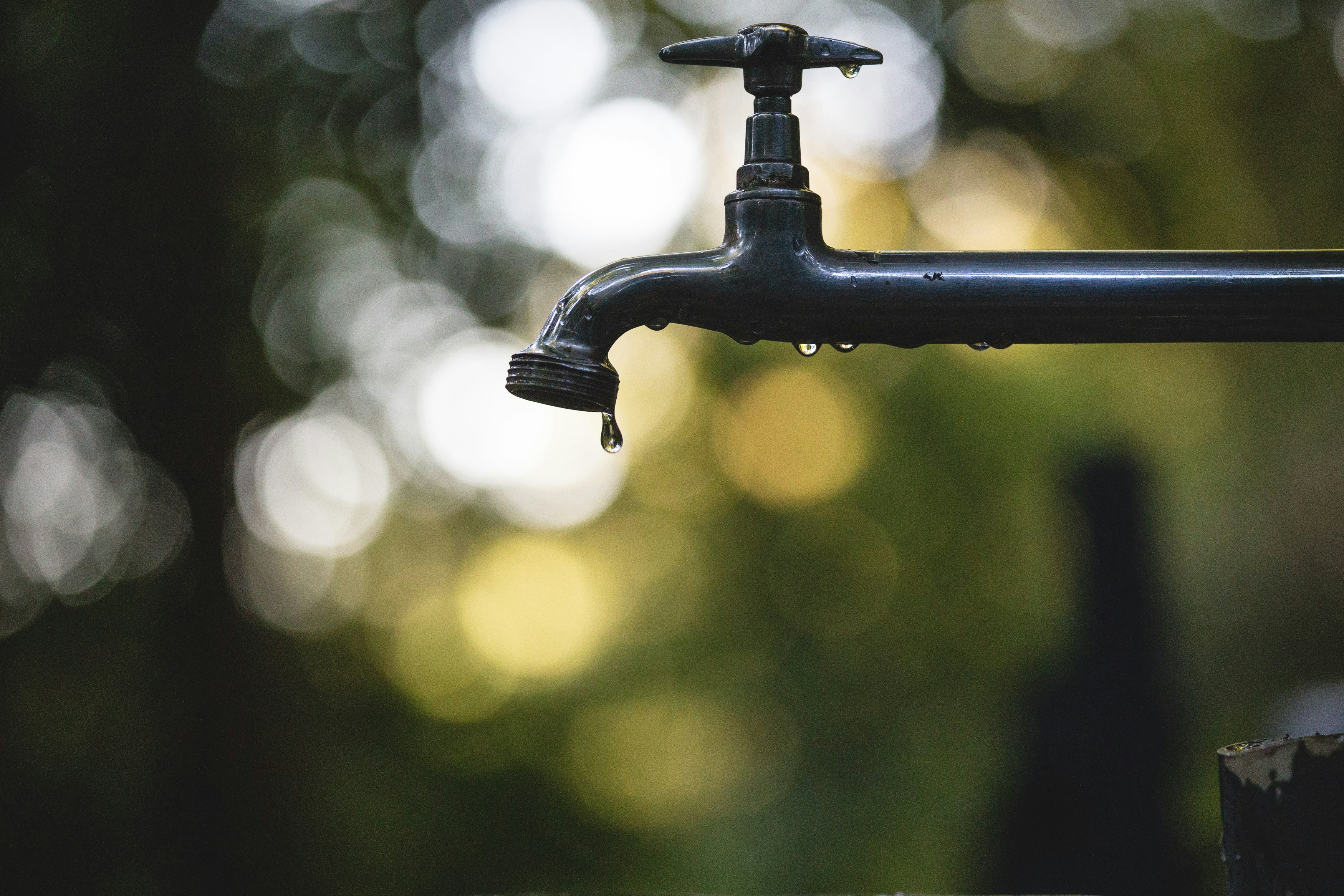 The image shows a water spigot with one drop falling out