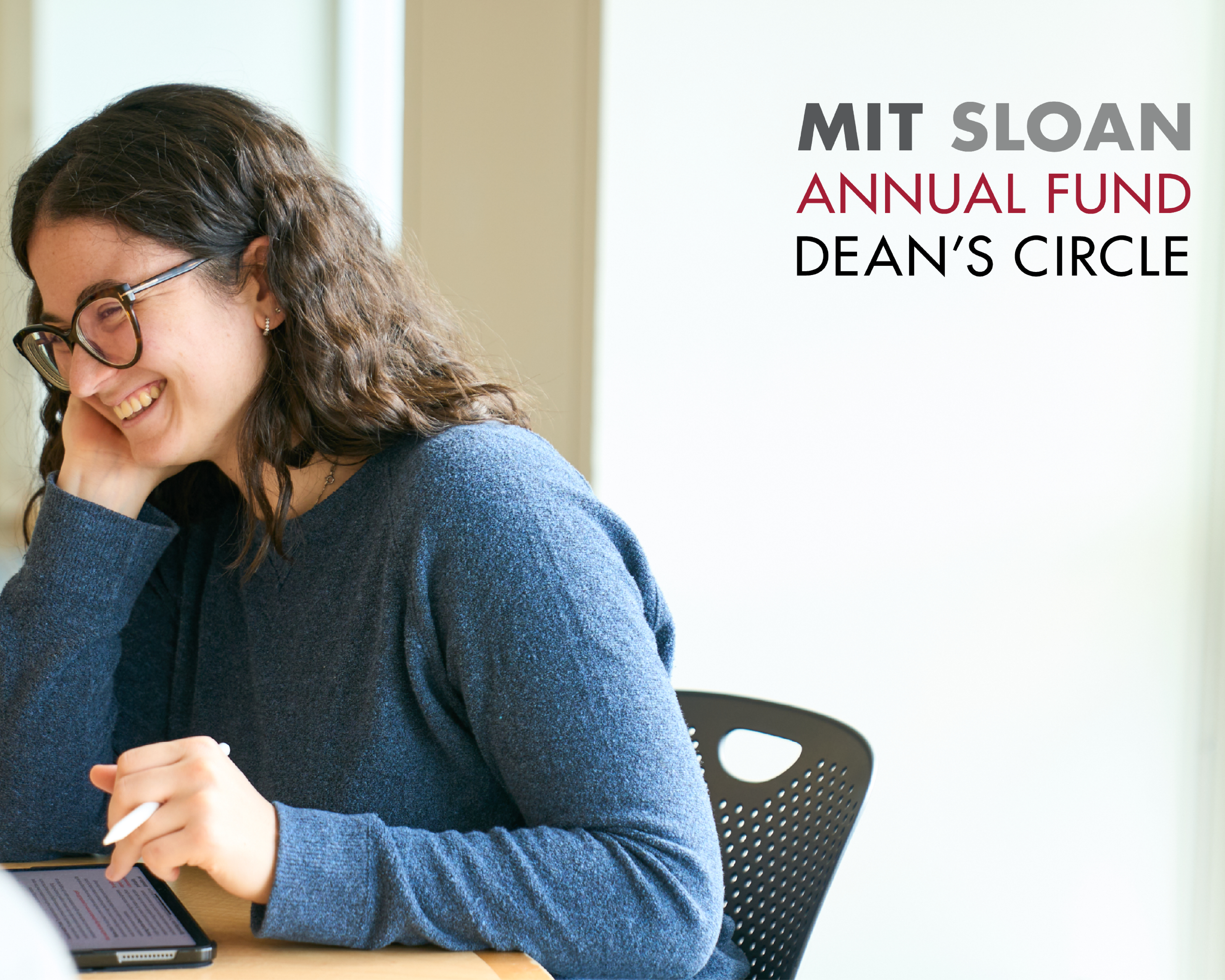 A woman smiles while working from a tablet and sitting at a table