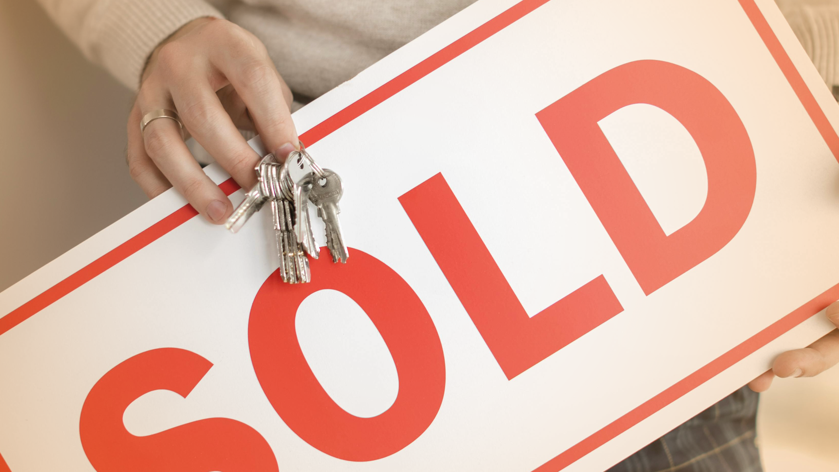 Person holding keys and a "Sold" sign